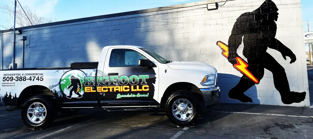 Bigfoot Electric's wrapped pickup in front of the painted Bigfoot mural with a lightning bolt